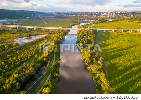 An aerial view of the Lahovice Bridge spanning the Berounka River, surrounded by lush greenery under a cloudy sky. Prague, Czechia An aerial view of the Lahovice Bridge spanning the Berounka River, surrounded by lush greenery under a cloudy sky. Prague, Czechia 128166310