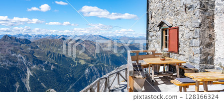 A tranquil scene at the Julius Payer House, showcasing a terrace with wooden benches and tables, affording visitors breathtaking views of the Italian Eastern Alps. Ortles Mountain, Italy 128166324