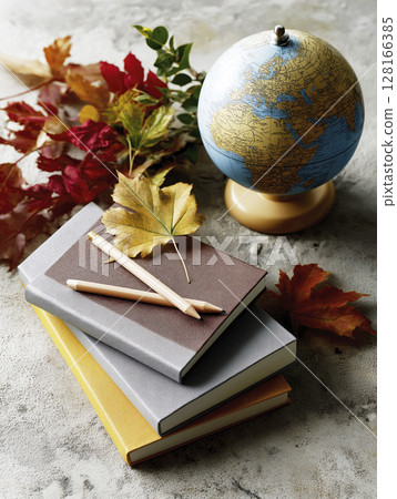 Colorful notebooks stacked with autumn leaves and a globe, perfect for back to school inspiration 128166385