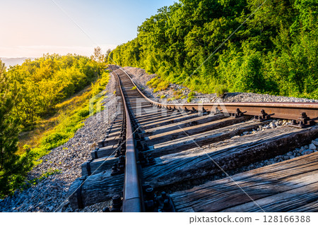 A railway line in Zagrad, Croatia suffers significant damage from a landslide, with bent tracks and debris scattered. The lush greenery surrounds the affected area, highlighting the disruption. 128166388