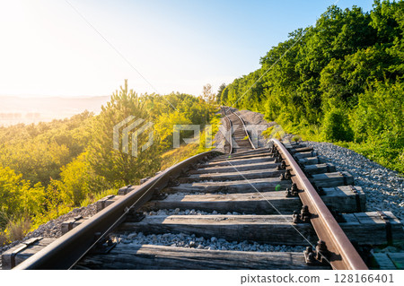 Railway tracks in Zagrad, Croatia, are damaged due to a recent landslide. Vegetation surrounds the area as the sun rises, highlighting the disruption in transportation. Railway tracks in Zagrad, Croatia, are damaged due to a recent landslide. Vegetation surrounds the area as the sun rises, highlighting the disruption in transportation. 128166401