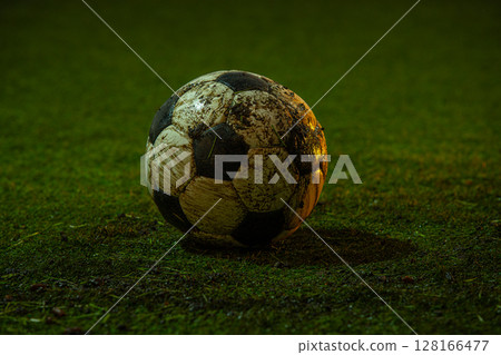 Dirty soccer ball lying on green grass field in evening stadium light Dirty soccer ball lying on green grass field in evening stadium light 128166477