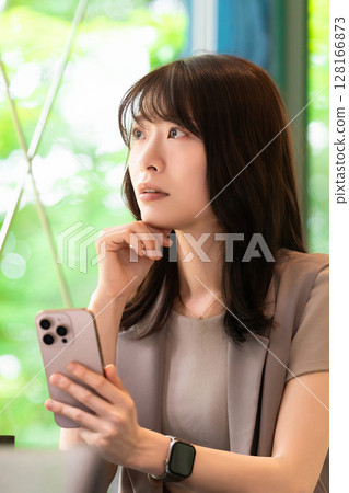 A woman thinking while using a smartphone in a cafe 128166873