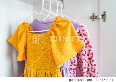 A close-up view of brightly colored children's clothes on hangers in a white wardrobe 128167074