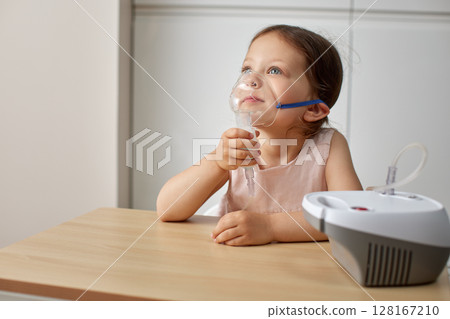 cute little toddler girl inhaling medicine on nebulizer and holding it on her own 128167210