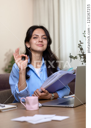 Happy woman showing okay sign gesture sitting at the desk and using laptop. Lady recommending online education 128167255