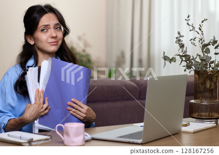 portrait of woman in blue shirt holds folders uses laptop in home office portrait of woman in blue shirt holds folders uses laptop in home office 128167256