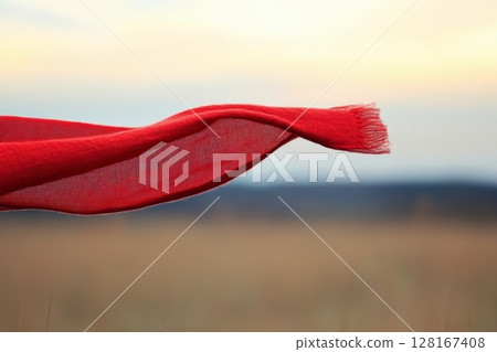Flowing red scarf dances in the wind against a serene landscape at sunset 128167408