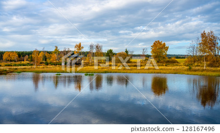 The tranquil Pernink peat bog in the Ore Mountains showcases vibrant autumn colors. Trees line the water's edge, reflecting beautifully in the calm surface under a partly cloudy sky. The tranquil Pernink peat bog in the Ore Mountains showcases vibrant autumn colors. Trees line the water's edge, reflecting beautifully in the calm surface under a partly cloudy sky. 128167496