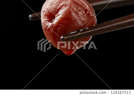 Close-up of a pickled plum being picked up by chopsticks Close-up of a pickled plum being picked up by chopsticks 128167513