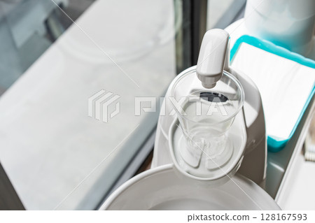 A plastic glass on a cup holder of the modern ceramic mouth cleaning sink in the dentist office near a window, A plastic glass on a cup holder of the modern ceramic mouth cleaning sink in the dentist office near a window, 128167593