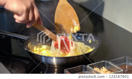 A cook stirs fry Pad Thai noodles in a pan with spatulas on electric stoves. Sauce dishes for cooking traditional Pad Thai. A cook stirs fry Pad Thai noodles in a pan with spatulas on electric stoves. Sauce dishes for cooking traditional Pad Thai. 128167601