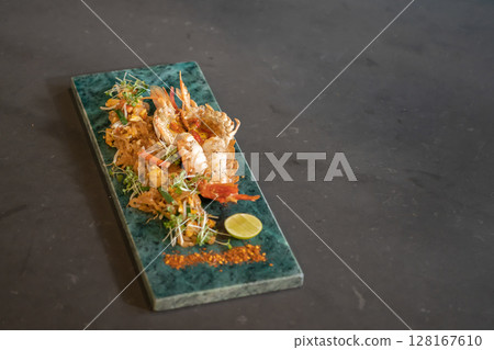 Lobster Pad Thai is served with yellow noodle, fried tofu, cress, bean sprouts, chilli power, garlic chives, and lime put on a rectangular plate. Lobster Pad Thai is served with yellow noodle, fried tofu, cress, bean sprouts, chilli power, garlic chives, and lime put on a rectangular plate. 128167610