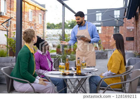 A waiter takes an order from customers at an outdoor restaurant. A waiter takes an order from customers at an outdoor restaurant. 128169211