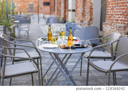 An outdoor restaurant setting featuring tables, chairs, drinks, and food. No people are visible. An outdoor restaurant setting featuring tables, chairs, drinks, and food. No people are visible. 128169242