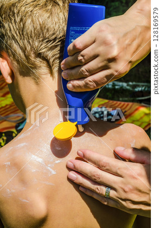 Parent applying sunscreen lotion from bottle on childs back for sun safety. High quality photo 128169579