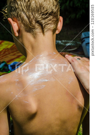 Applying sunscreen on boys back for sun protection on summer outdoor day. High quality photo 128169585