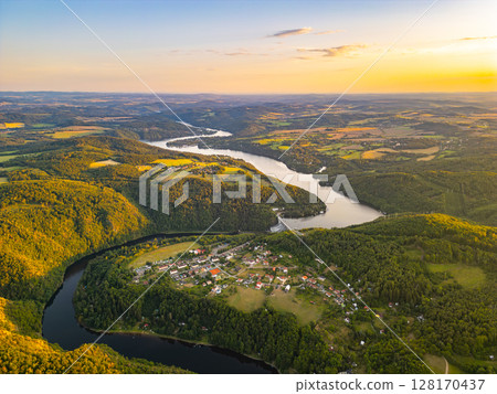 A breathtaking sunset illuminates the Slapy Water Reservoir, showcasing the serene landscape and vibrant colors. The tranquil waters reflect the hues of dusk, enhancing the natural beauty of the area. A breathtaking sunset illuminates the Slapy Water Reservoir, showcasing the serene landscape and vibrant colors. The tranquil waters reflect the hues of dusk, enhancing the natural beauty of the area. 128170437