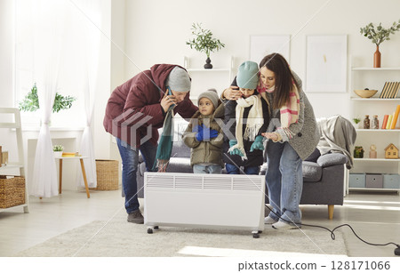 Freezing family in warm clothes standing by electric heater, calling emergency services for help. 128171066