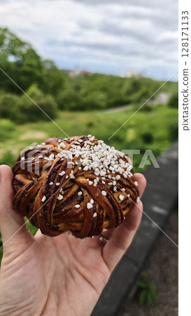 Traditional Swedish cinnamon bun with pearl sugar held outdoors against a green natural background. This image represents a sweet treat and cozy Scandinavian fika concept Traditional Swedish cinnamon bun with pearl sugar held outdoors against a green natural background. This image represents a sweet treat and cozy Scandinavian fika concept 128171133