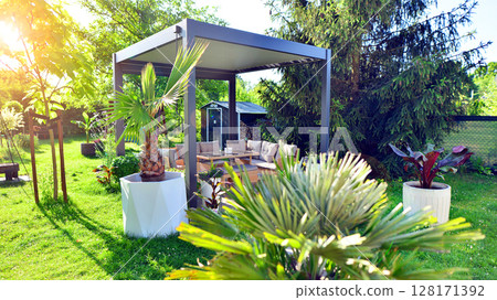 Modern aluminum pergola with stylish garden furniture in a beautiful garden. 128171392