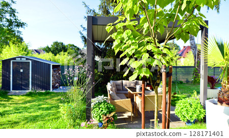 Modern aluminum pergola with stylish garden furniture in a beautiful garden. 128171401