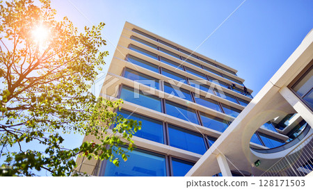 City life, urban landscape and ecology. Modern office complex with glass facades and smooth lines against backdrop of green trees, concept of modern architecture. Organically building into nature. City life, urban landscape and ecology. Modern office complex with glass facades and smooth lines against backdrop of green trees, concept of modern architecture. Organically building into nature. 128171503