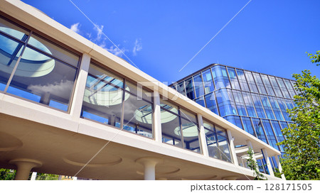City life, urban landscape and ecology. Modern office complex with glass facades and smooth lines against backdrop of green trees, concept of modern architecture. Organically building into nature. City life, urban landscape and ecology. Modern office complex with glass facades and smooth lines against backdrop of green trees, concept of modern architecture. Organically building into nature. 128171505