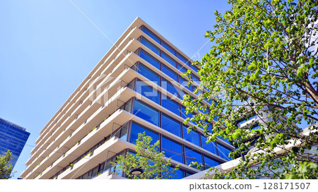 City life, urban landscape and ecology. Modern office complex with glass facades and smooth lines against backdrop of green trees, concept of modern architecture. Organically building into nature. City life, urban landscape and ecology. Modern office complex with glass facades and smooth lines against backdrop of green trees, concept of modern architecture. Organically building into nature. 128171507