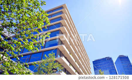 City life, urban landscape and ecology. Modern office complex with glass facades and smooth lines against backdrop of green trees, concept of modern architecture. Organically building into nature. City life, urban landscape and ecology. Modern office complex with glass facades and smooth lines against backdrop of green trees, concept of modern architecture. Organically building into nature. 128171508