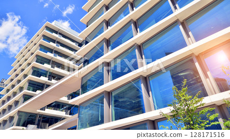 City life, urban landscape and ecology. Modern office complex with glass facades and smooth lines against backdrop of green trees, concept of modern architecture. Organically building into nature. City life, urban landscape and ecology. Modern office complex with glass facades and smooth lines against backdrop of green trees, concept of modern architecture. Organically building into nature. 128171516