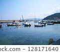 A serene and picturesque view of boats gently floating in the calm waters of the port on Elba Island, Italy. Surrounded by pastel-colored buildings and rugged coastal hills, the tranquil harbor scene 128171640