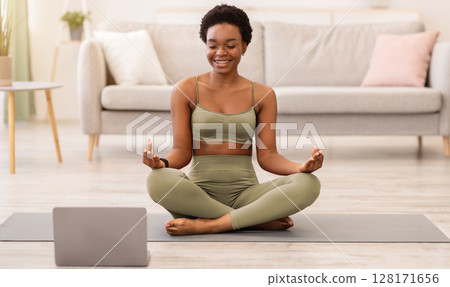 Online Yoga. Happy Black Woman Meditating Sitting In Lotus Position On Floor, Relaxing At Laptop Computer At Home. Meditation And Relaxation Leisure Concept. Selective Focus 128171656