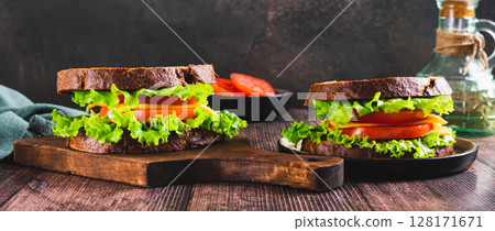 Vegetarian sandwich with tomato, cheese and lettuce on a board on a table web banner Vegetarian sandwich with tomato, cheese and lettuce on a board on a table web banner 128171671