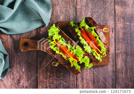 Close up of vegetarian sandwich with tomato, cheese and lettuce on a board top view Close up of vegetarian sandwich with tomato, cheese and lettuce on a board top view 128171673