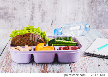 Lunch box with food, bottle of water, notebook and pen on the table Lunch box with food, bottle of water, notebook and pen on the table 128171681