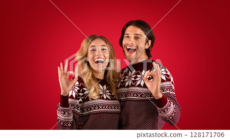 Xmas time. Excited girl with her boyfriend showing OK gestures on red background, panorama Xmas time. Excited girl with her boyfriend showing OK gestures on red background, panorama 128171706
