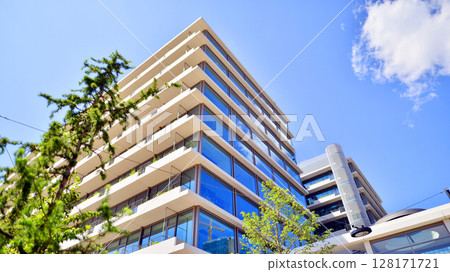 City life, urban landscape and ecology. Modern office complex with glass facades and smooth lines against backdrop of green trees, concept of modern architecture. Organically building into nature. City life, urban landscape and ecology. Modern office complex with glass facades and smooth lines against backdrop of green trees, concept of modern architecture. Organically building into nature. 128171721