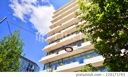 City life, urban landscape and ecology.  Modern office complex with glass facades and smooth lines against backdrop of green trees, concept of modern architecture. Organically building into nature.   City life, urban landscape and ecology.  Modern office complex with glass facades and smooth lines against backdrop of green trees, concept of modern architecture. Organically building into nature.   128171743