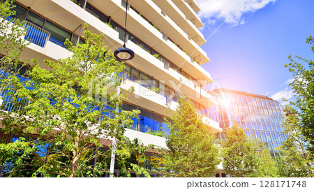 City life, urban landscape and ecology. Modern office complex with glass facades and smooth lines against backdrop of green trees, concept of modern architecture. Organically building into nature. City life, urban landscape and ecology. Modern office complex with glass facades and smooth lines against backdrop of green trees, concept of modern architecture. Organically building into nature. 128171748