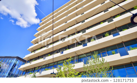 City life, urban landscape and ecology. Modern office complex with glass facades and smooth lines against backdrop of green trees, concept of modern architecture. Organically building into nature. City life, urban landscape and ecology. Modern office complex with glass facades and smooth lines against backdrop of green trees, concept of modern architecture. Organically building into nature. 128171753