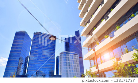 City life, urban landscape and ecology.  Modern office complex with glass facades and smooth lines against backdrop of green trees, concept of modern architecture. Organically building into nature.   128171757