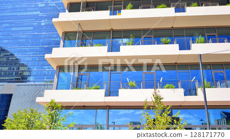 City life, urban landscape and ecology.  Modern office complex with glass facades and smooth lines against backdrop of green trees, concept of modern architecture. Organically building into nature.   128171770