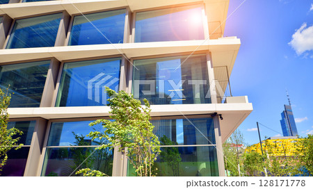 City life, urban landscape and ecology.  Modern office complex with glass facades and smooth lines against backdrop of green trees, concept of modern architecture. Organically building into nature.   128171778