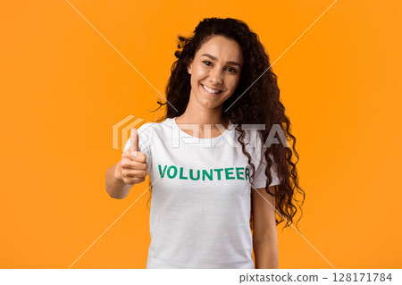 Volunteer Woman Showing Like Gesturing Thumbs Up Standing On Yellow Studio Background, Smiling To Camera. I Approve Charity Work And Volunteering Concept 128171784