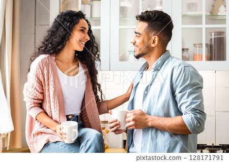 Loving Middle Eastern Couple Bonding While Drinking Coffee In Kitchen, Happy Millennial Arab Man And Woman Holding Cups With Hot Drinks And Enjoying Spending Time Together At Home, Closeup 128171791