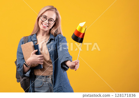 Tourist traveling, trip and learning Deutsche language. Teen happy female in glasses with notebooks and backpack waving small flag of Germany, isolated on beige background, studio shot, empty space 128171836