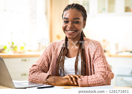 Distance Job. Portrait Of Happy Black Freelancer Lady Sitting At Table With Laptop, Cheerful African American Woman Working Online On Computer At Desk In Kitchen, Smiling At Camera, Free Space Distance Job. Portrait Of Happy Black Freelancer Lady Sitting At Table With Laptop, Cheerful African American Woman Working Online On Computer At Desk In Kitchen, Smiling At Camera, Free Space 128171851