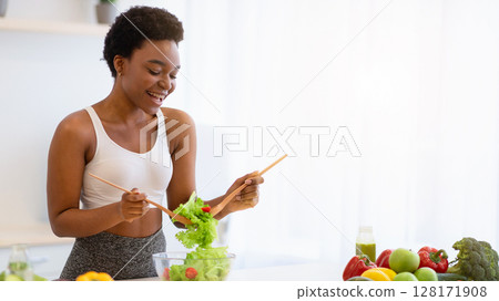 Cheerful Fit Black Woman Cooking Fresh Vegetable Salad Standing In Modern Kitchen Indoor. Healthy Eating, Dieting Nutrition For Slimming And Weight Loss Concept. Copy Space Cheerful Fit Black Woman Cooking Fresh Vegetable Salad Standing In Modern Kitchen Indoor. Healthy Eating, Dieting Nutrition For Slimming And Weight Loss Concept. Copy Space 128171908