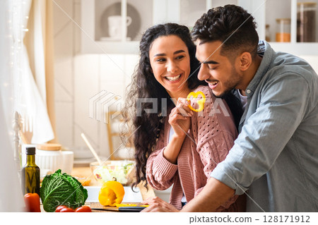 Cheerful Arab Couple Having Fun While Cooking Healthy Lunch Together In Kitchen, Romantic Young Middle Eastern Spouses Laughing While Preparing Tasty Vegetable Meal At Home, Copy Space 128171912